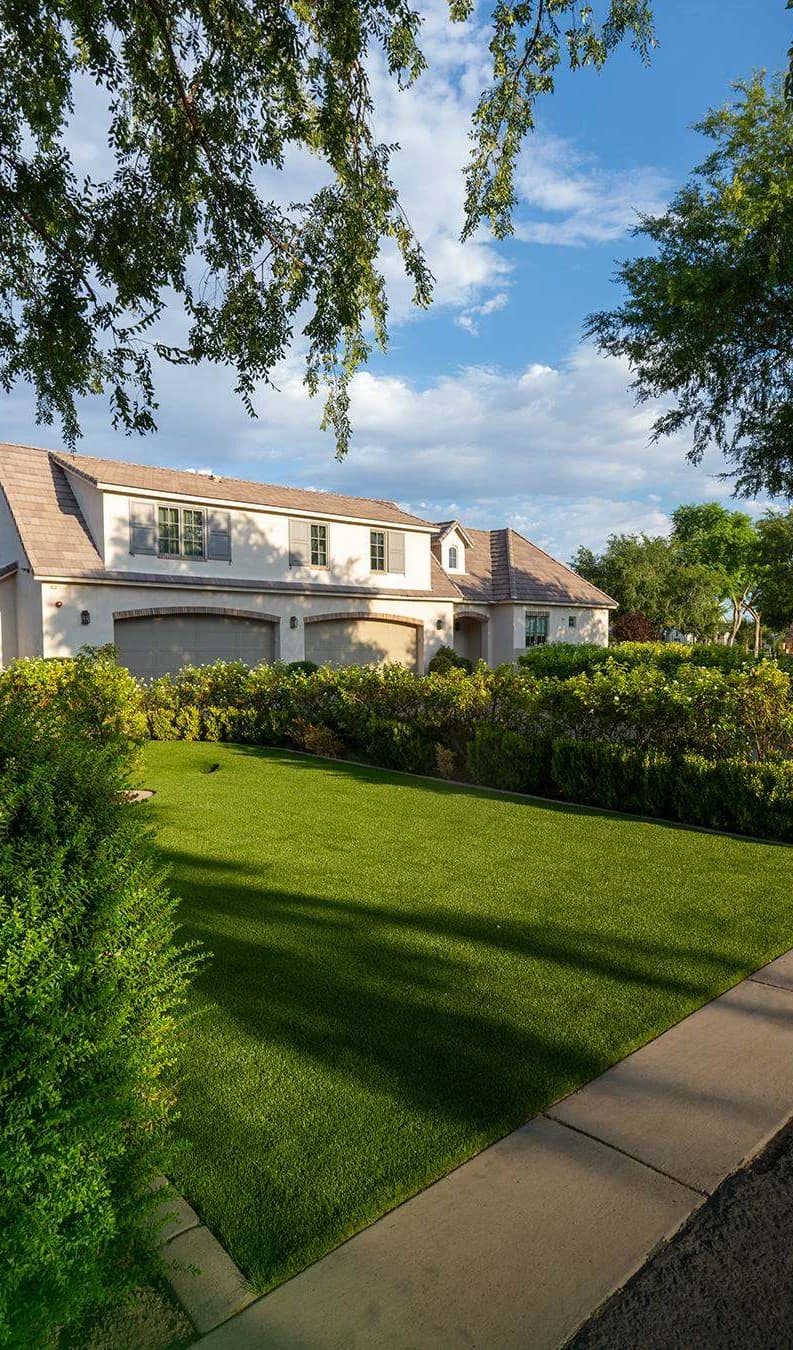 A TurfIt front lawn along the sidewalk, hedges and a two storey house behind
