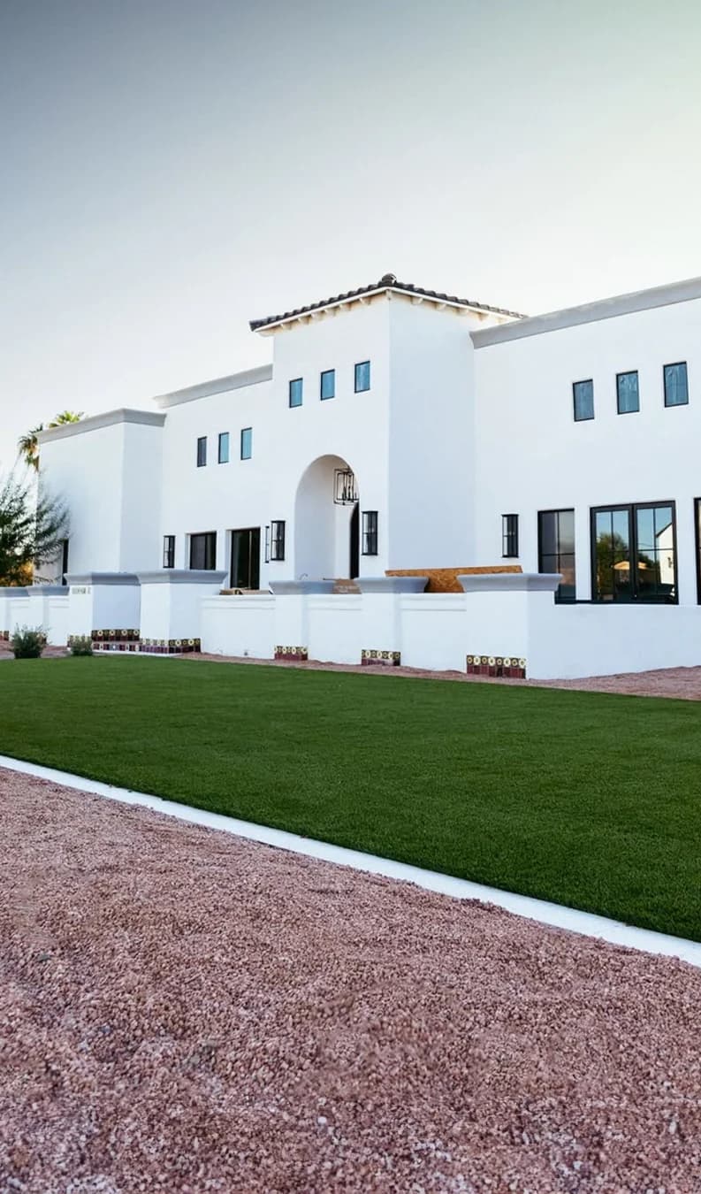 A TurfIt lawn in front of a white stucco house, a red gravel border in the foreground